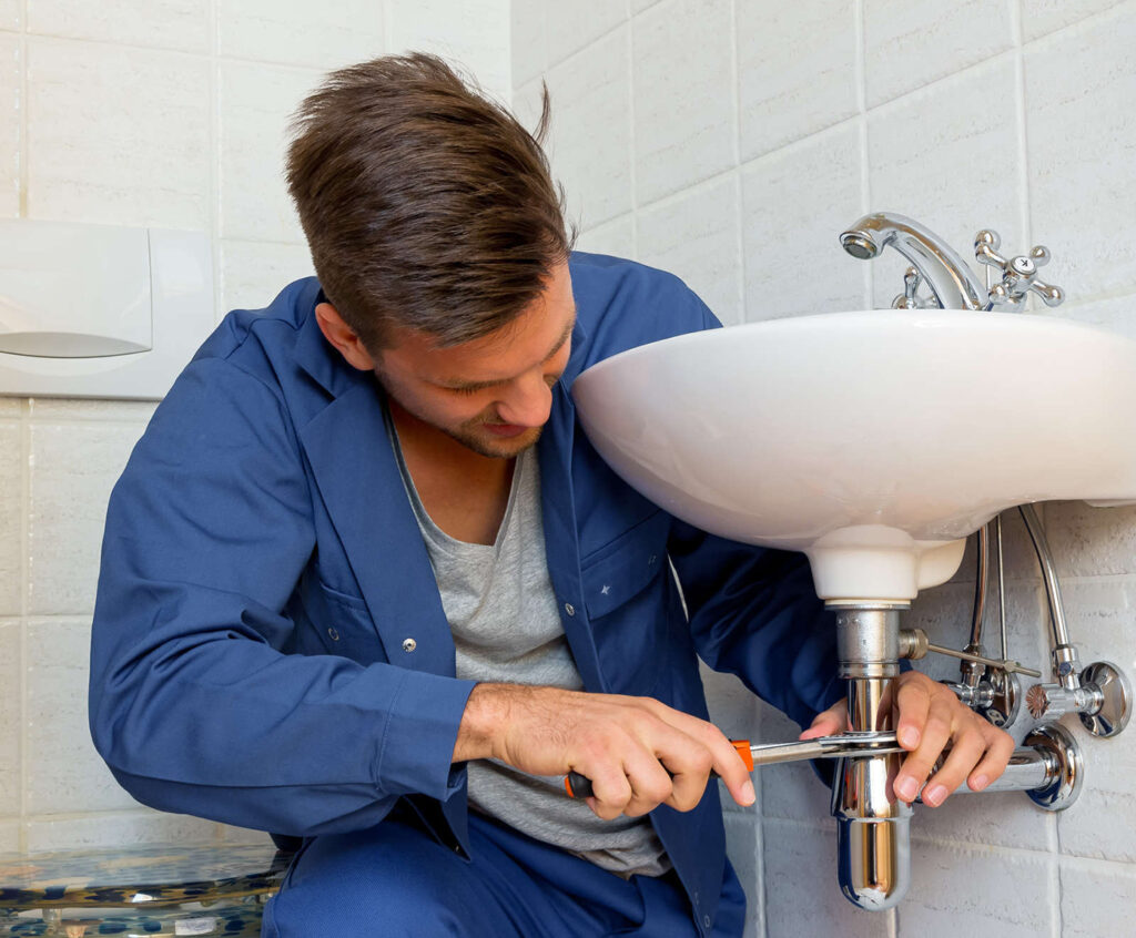 plombier avec chemise bleu répare un lavabo